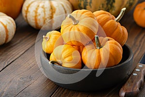 Several small pumpkins in a wooden bowl on kitchen table