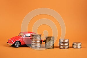 Several stacks of coins and a small red car on a brown background, buying and selling a car concept