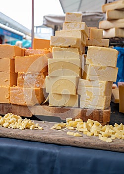Several stacks of various flavours of cheddar cheese for sale on a market stall with small cubes for tasting in the foreground