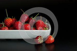 Several strawberries are housed in white ceramic vessels and placed on a black floor.