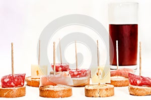 Several toothpicks holding toast with cheese and ham and glass with vermouth