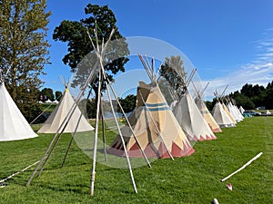 Several traditional teepees have been set up at a festival.Skeletal frame of wooden poles seen in the foreground.