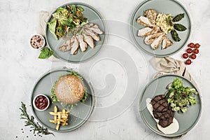 Several warm dishes with chicken, turkey, beef fillets and pork cutlet burgers in different plates