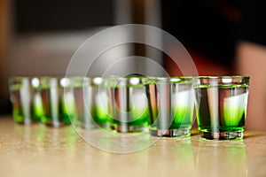 Several white-green alcoholic drinks shots on the bar counter. Close-up, selective focus