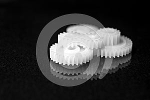 Several white plastic gears on a black mirror background. Mechanical repair. Fix. Reflection. Repair shop. Cogwheels. Elements of