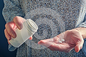 Several white round tablets (vitamins) on a woman's palm, a white plastic bottle for pills in her hand.