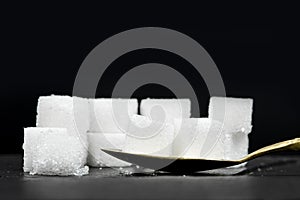 Several white sugar cubes were placed in a brass spoon on a black stone background