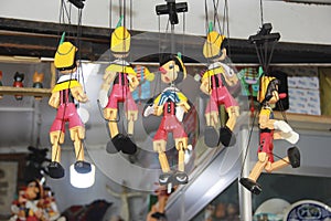 Several wooden pinocchio puppets in colorful costumes hanging on a rope on sale in the store