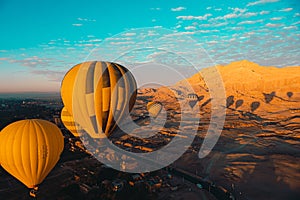 Several yellow and orange hot air balloons in luxor egypt, during early takeoff at low height. Amazing sandy area in the distance