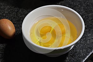 Several yolks and white egg into a ceramic bowl beside a brown egg