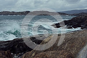 Severe gloomy norway landscape with stormy sea - grey waves of Arctic Ocean in gale and black granite rocks in cloudy weather.