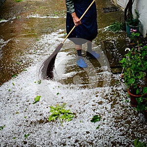 Older non recognisable woman sweeping up hailstones in courtyard after hailstone storm