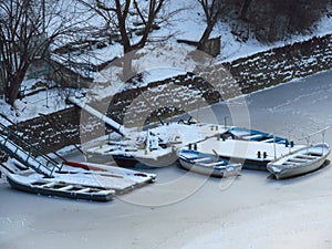 Severe freezing winter. Small boats frozen in water near by the coast. Frozen river, pond, lake, sea.