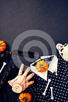 Severed hand Thing from Addams Family, Wednesday dress and hair braids, spiders, bones, orange pumpkins on dark background.