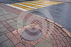 Sewer cast iron manholes on sidewalk. Wet metal is covered with yellow autumn leaves after rain