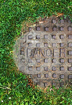 Sewer manhole with grass and word danger