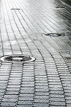 Sewer manhole on wet cobblestone street