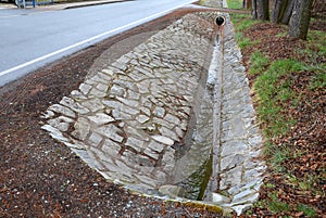 Sewer pipes under the bridge. crossing the ditch by the road. concrete hole with stone paving surroundings. The gutter drains arou