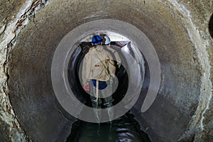 Sewer tunnel worker examines sewer system damage and wastewater leakage photo