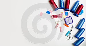 Sewing accessories: many spools of red and blue thread, pins,chalks,tape and other sewing tools on a white background with copy