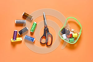 Sewing accessories scissors, handbag, spools with colorful threads and needles on orange tailors desk in workshop