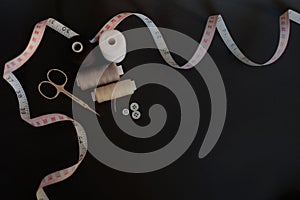 Sewing accessories scissors, measuring tape, thread, buttons on black background with place for text. Flat lay