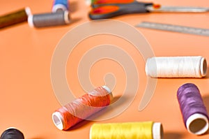 Sewing accessories scissors, metal ruler, spools with colorful threads on orange tailors desk in workshop