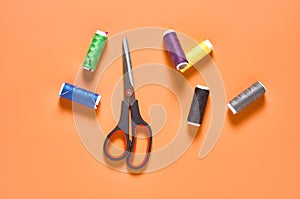 Sewing accessories scissors and spools with colorful threads and needles on orange tailors desk in workshop