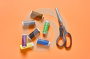 Sewing accessories scissors and spools with colorful threads and needles on orange tailors desk in workshop