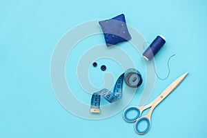 Sewing accessories with threads, scissors, pins, fabric, buttons and sewing tape on blue background. Top view. Flat lay