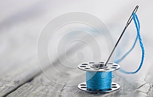 sewing bobbin with blue thread and needle.