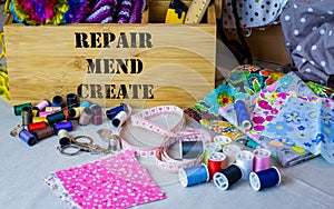 Sewing box with repair, mend and create text surrounded by sewing tools, fabric and thread.