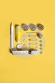 Sewing kit accessories and tools for needle work in yellow. Tape measure, pins, scissors, buttons, prewound bobbins, thimble,