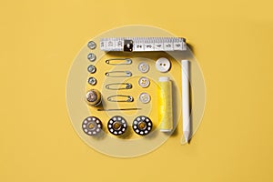 Sewing kit accessories and tools for needle work in yellow. Tape measure, pins, scissors, buttons, prewound bobbins, thimble,