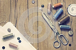 Sewing kit. Scissors, bobbins with thread and needles on the old wooden background