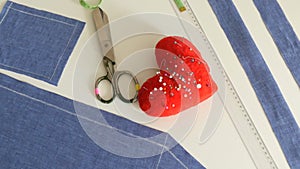Sewing kit, sewing scissors, scraps of blue fabric, a red pin cushion with needles in the form of a heart, a centimeter