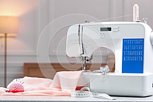 Sewing machine with fabric and other supplies on white table in workshop, space for text