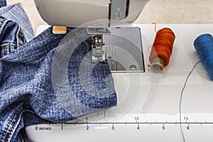 Sewing machine foot on denim. Scissors, spools of thread. Stands on a table
