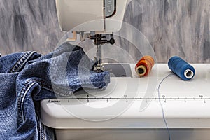 Sewing machine foot on denim. Scissors, spools of thread. Stands on a table