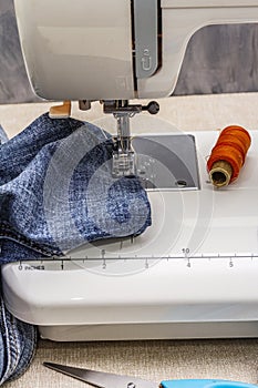 Sewing machine foot on denim. Scissors, spools of thread. Stands on a table