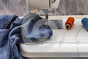 Sewing machine foot on denim. Scissors, spools of thread. Stands on a table