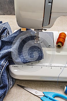 Sewing machine foot on denim. Scissors, spools of thread. Stands on a table