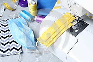 Sewing machine, homemade protective masks and craft accessories on grey table