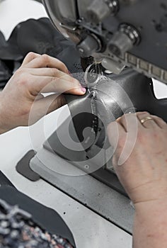 Sewing machine in a leather workshop in action with hands working on a leather details for shoes. Old women`s hands with