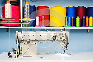 Sewing machine overlock in tailor workshop on the background of a shelf with colorful threads