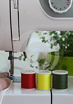 The sewing machine`s foot with a needle sews ecru fabric. Sewing machine details - vertical image