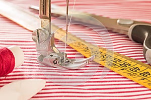 The sewing machine`s foot with a needle sews fabric