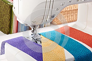 Sewing machine with a strips of fabrics on the background of stack of colorful quilting fabrics