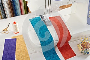 Sewing machine with a strips of fabrics on the background of stack of colorful quilting fabrics, sewing accessories