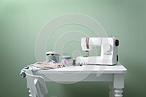 Sewing machine with tailor's accessories on table against color background